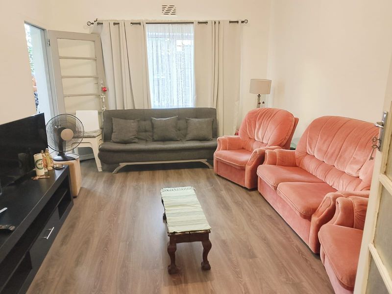 A living room featuring laminate flooring and a wall-mounted air vent, providing a functional and well-lit space.
