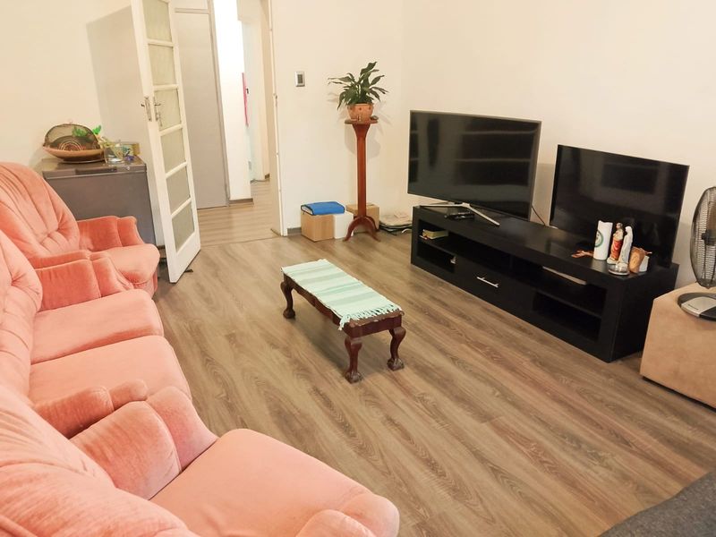 A living room featuring wood-look laminate flooring and access to an adjacent hallway.