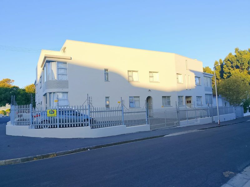 Exterior view of a multi-story apartment building featuring a secure perimeter with metal fencing, electric security wires, and a gated entrance.