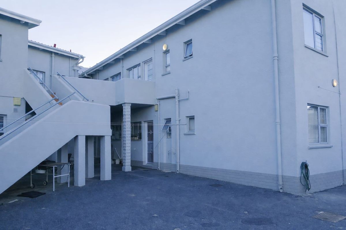 Rear view of the apartment building featuring an external staircase, balcony access, and paved ground area.