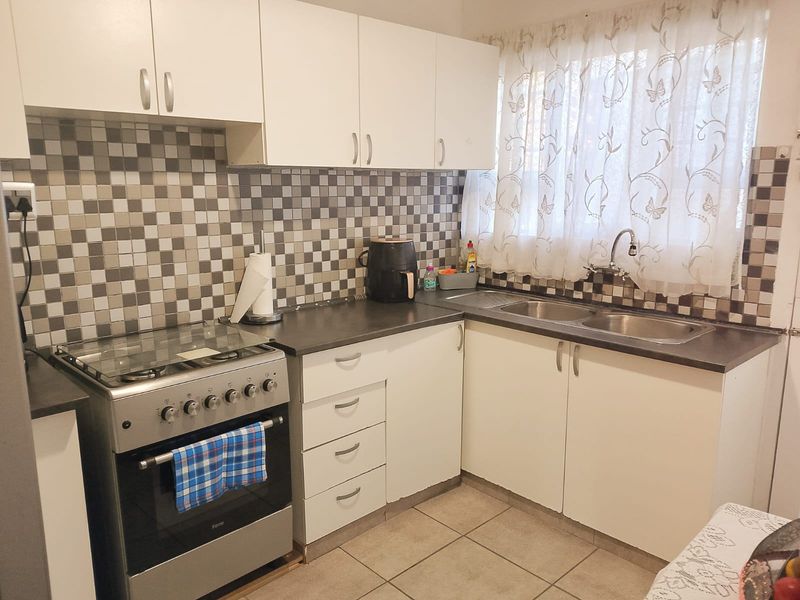 A functional kitchen featuring white cabinetry, mosaic tile backsplash, laminate countertops, a double bowl sink, and a freestanding stove.