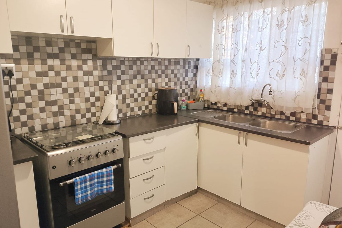 A functional kitchen featuring white cabinetry, mosaic tile backsplash, laminate countertops, a double bowl sink, and a freestanding stove.