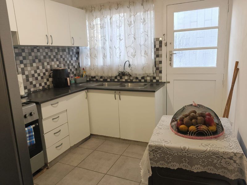 Functional kitchen featuring white cabinetry, tiled backsplash, double basin sink, and direct access to an external door.