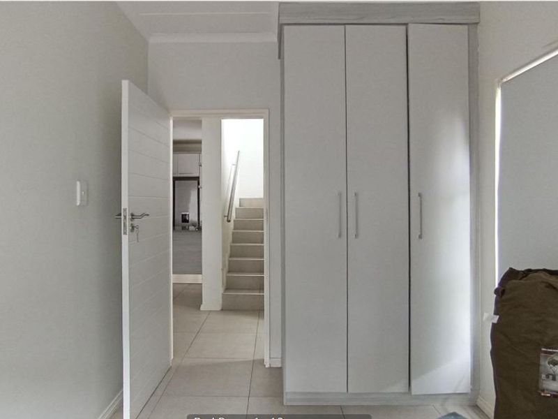 A bright, empty bedroom featuring neutral tiled flooring and modern built-in cupboards, with a view through the doorway to an internal staircase.