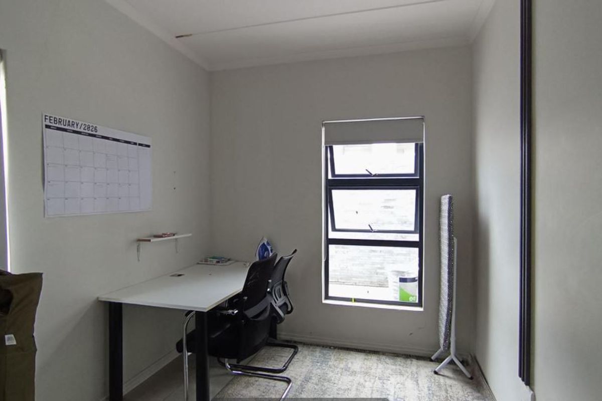 A functional bedroom or home office space featuring an aluminium window with a roller blind and neutral wall finishes.