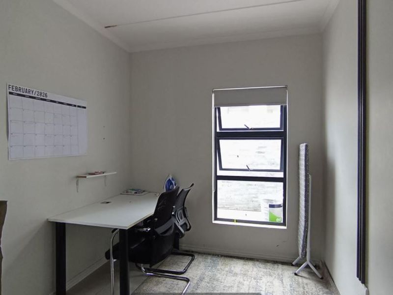 A functional bedroom or home office space featuring an aluminium window with a roller blind and neutral wall finishes.