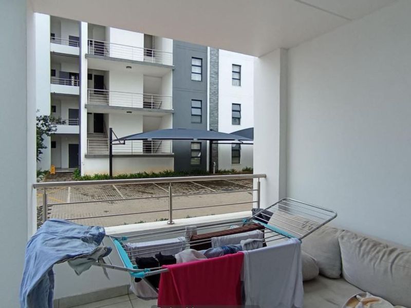 A covered balcony featuring tiled flooring, a stone-clad feature wall, and a stainless steel balustrade overlooking the complex parking area.