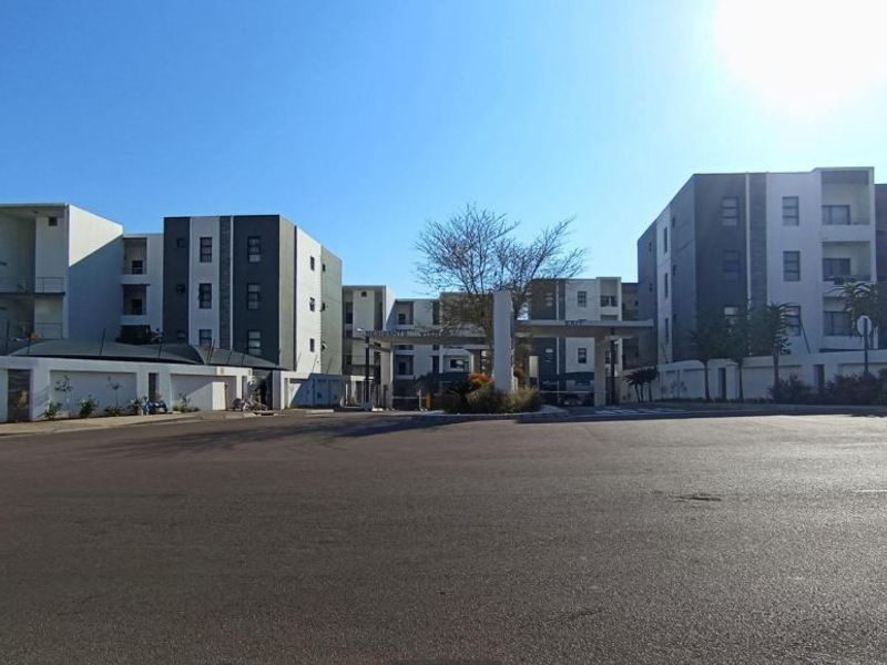 Street view of a modern multi-story residential complex featuring a gated entrance and secure perimeter wall.