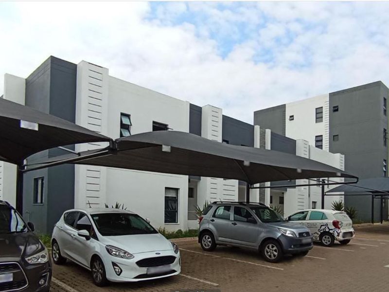 Exterior view of a modern multi-story residential complex featuring paved parking bays with shade cloth carports.