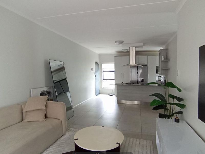 Modern open-plan living area featuring a contemporary kitchen with island, stainless steel extractor fan, and neutral tiled flooring throughout.