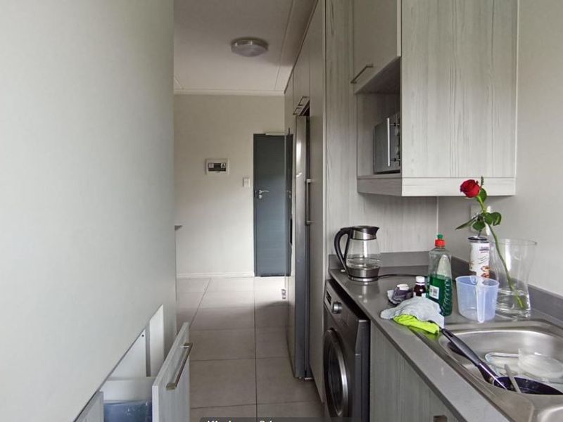 A functional scullery area featuring built-in cabinetry, a stainless steel sink, and integrated laundry appliances, providing efficient utility space.