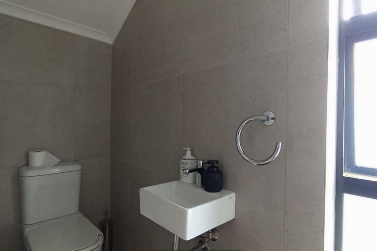 A modern, compact bathroom featuring neutral wall tiles, a wall-mounted basin with chrome fixtures, and a standard toilet.