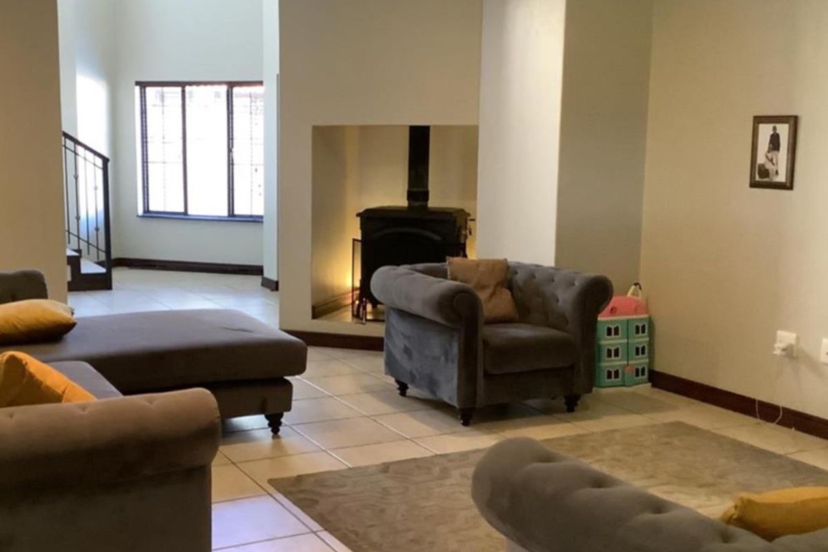 Spacious living area featuring tiled flooring, a central freestanding fireplace, and an open-plan layout with a staircase leading to the upper level.