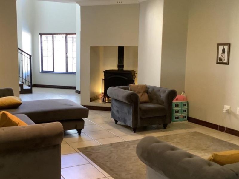 Spacious living area featuring tiled flooring, a central freestanding fireplace, and an open-plan layout with a staircase leading to the upper level.
