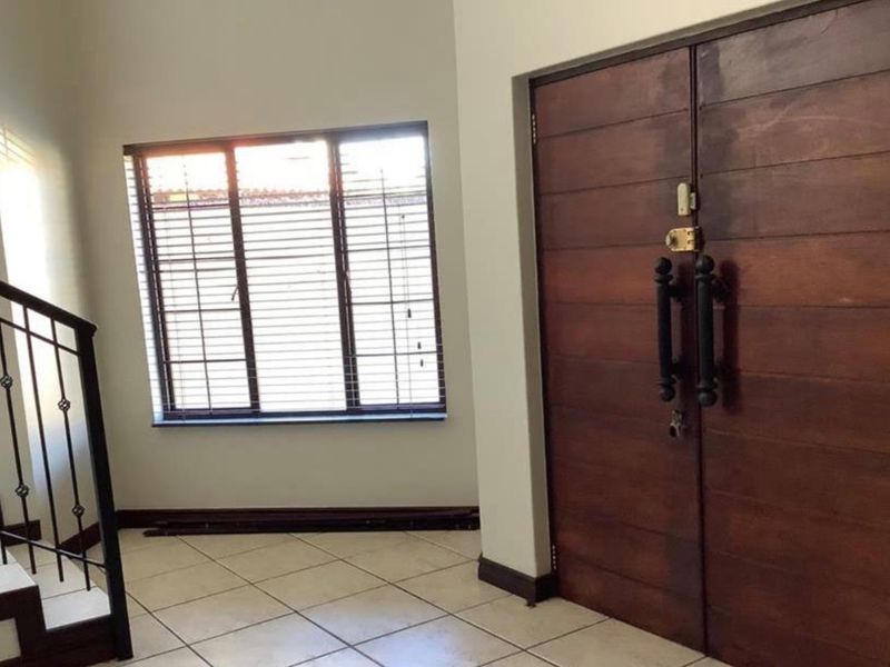 Spacious entrance foyer featuring double timber doors, ceramic tiled flooring, and a wrought iron staircase railing.