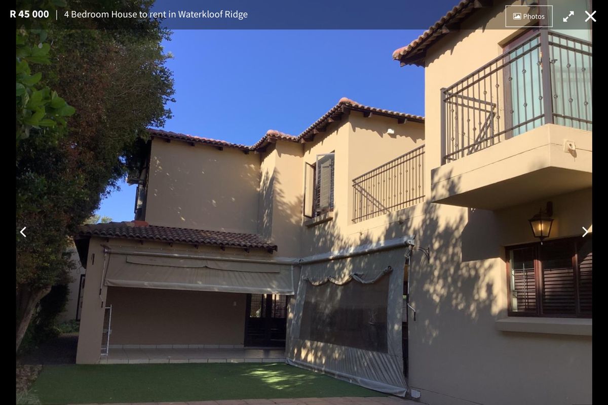 Rear view of the property featuring a covered patio area, balcony with wrought iron railings, swimming pool, and artificial lawn.