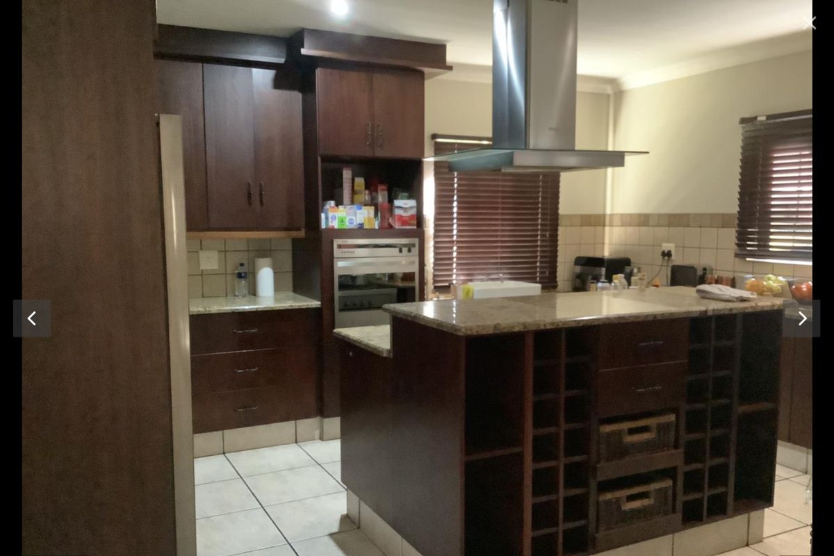 A functional kitchen featuring dark wood cabinetry, granite countertops, a built-in oven, and a stainless steel extractor fan with tiled flooring.