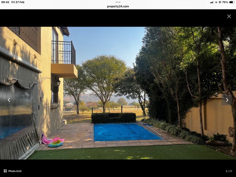 Rear garden area featuring a swimming pool with cover, paved patio, and a balcony overlooking the landscaped yard and surrounding landscape.