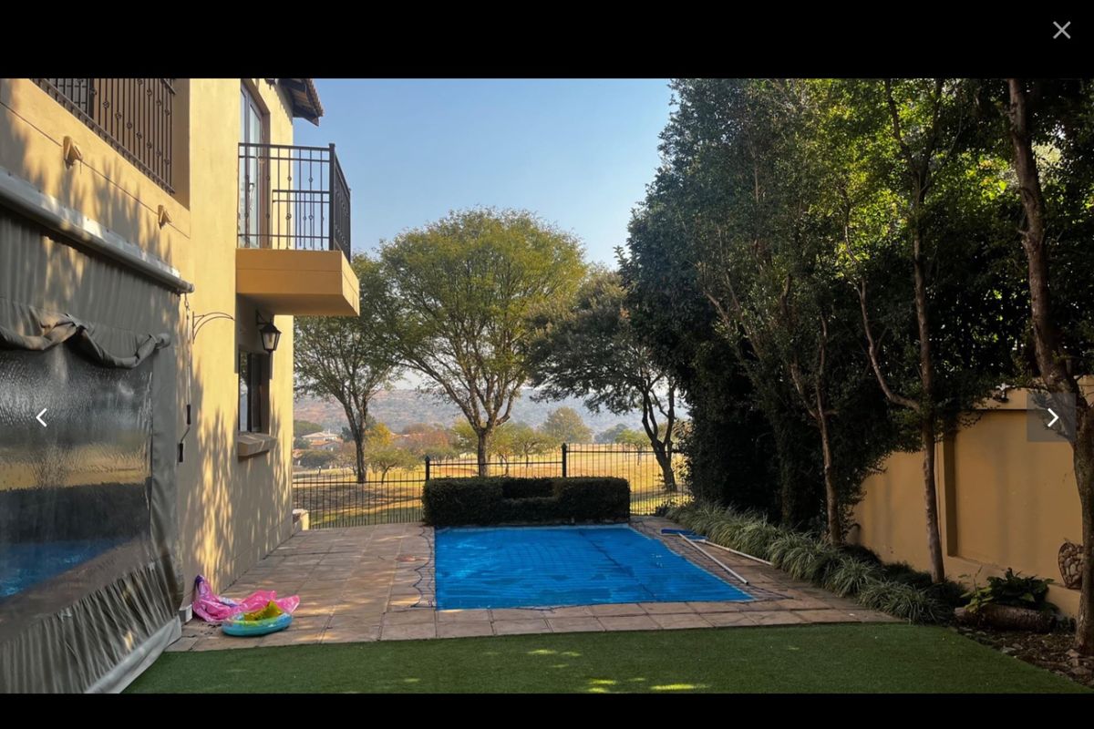 Rear garden area featuring a swimming pool with cover, paved patio, and a balcony overlooking the landscaped yard and surrounding landscape.