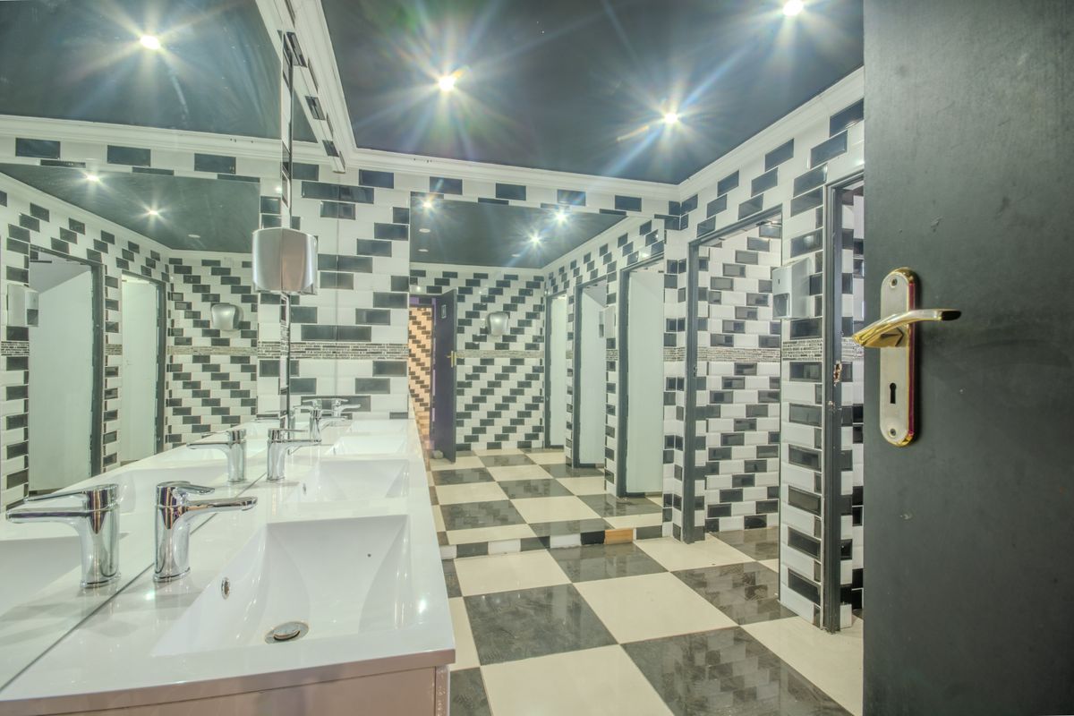 A spacious commercial bathroom featuring multiple vanity basins, large mirrors, and distinctive black and white tiled walls and flooring with multiple toilet cubicles.