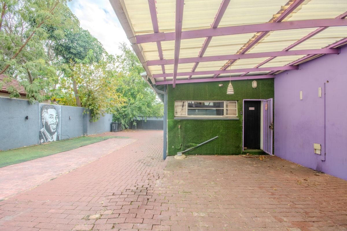 Rear exterior area featuring a paved driveway, covered patio space, and boundary wall with mural, providing functional outdoor access.