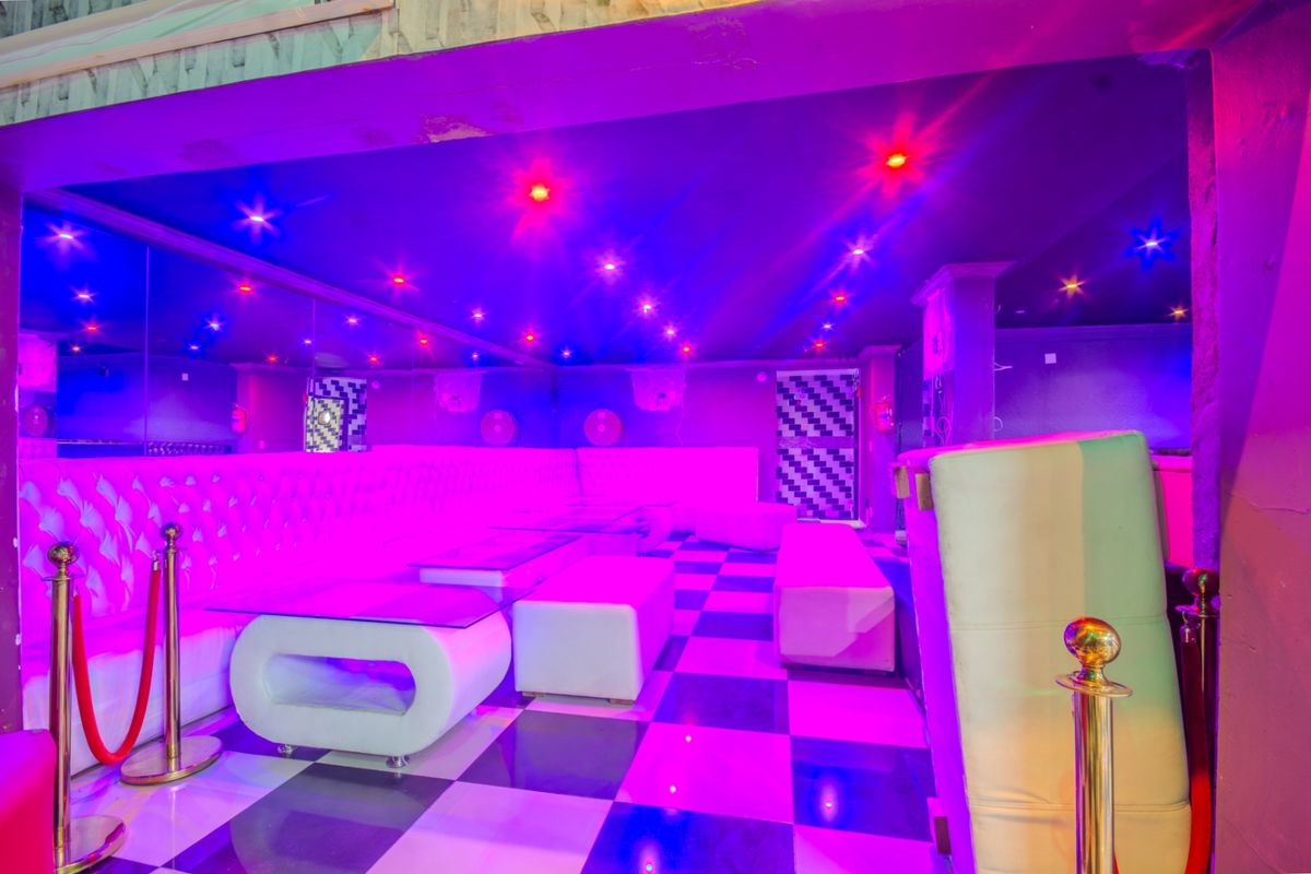 A vibrant commercial clubhouse or lounge area featuring checkered flooring, mirrored walls, built-in bench seating, and integrated recessed ceiling lighting with colorful ambient illumination.