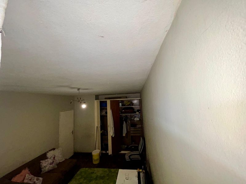 A bedroom featuring a built-in wardrobe and ceiling light fixture, currently showing signs of wear on the walls and ceiling.