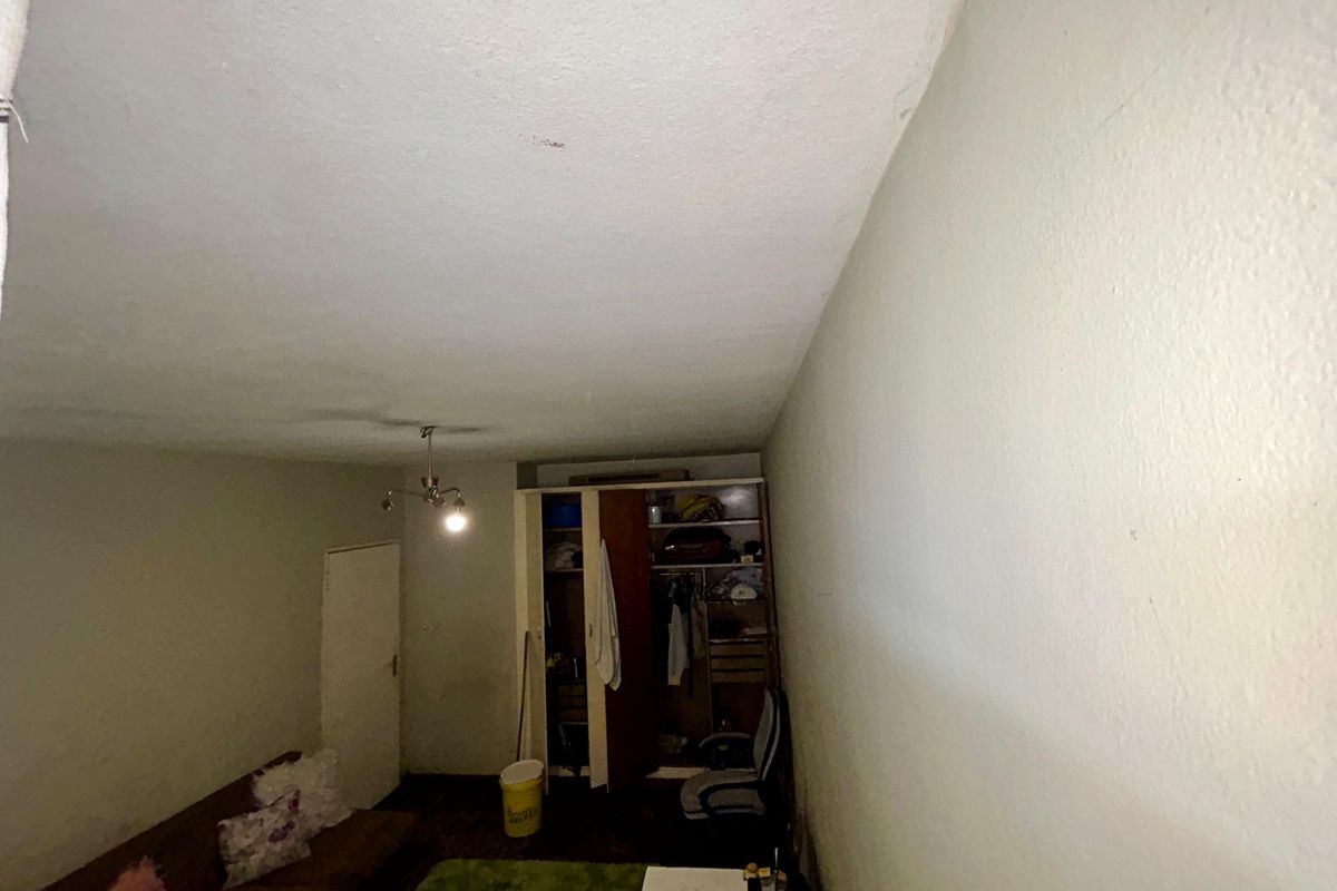 A bedroom featuring a built-in wardrobe and ceiling light fixture, currently showing signs of wear on the walls and ceiling.