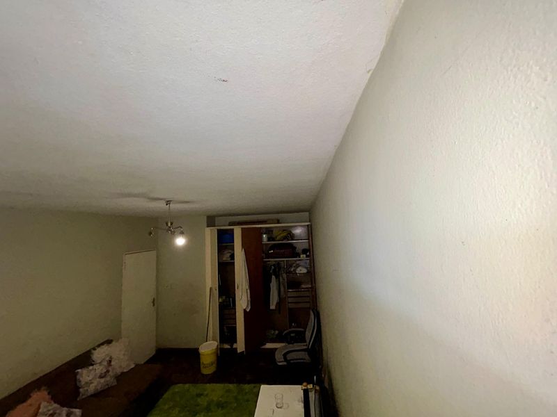A bedroom featuring a built-in wardrobe and basic lighting, currently showing signs of wear and requiring cosmetic updates to improve its overall condition.