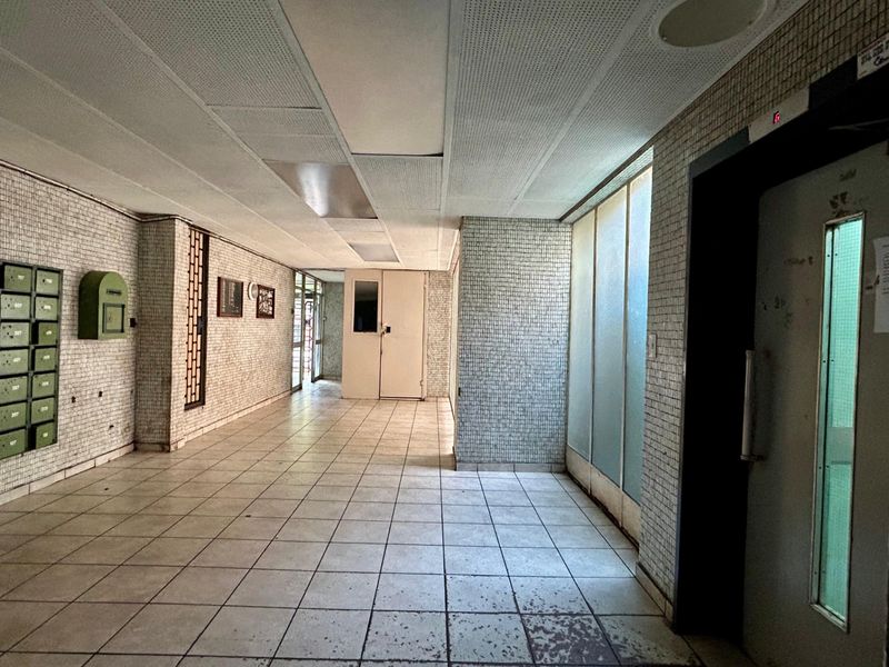 A communal apartment building entrance lobby featuring tiled walls and flooring, an elevator, and integrated mailboxes in a dated condition.