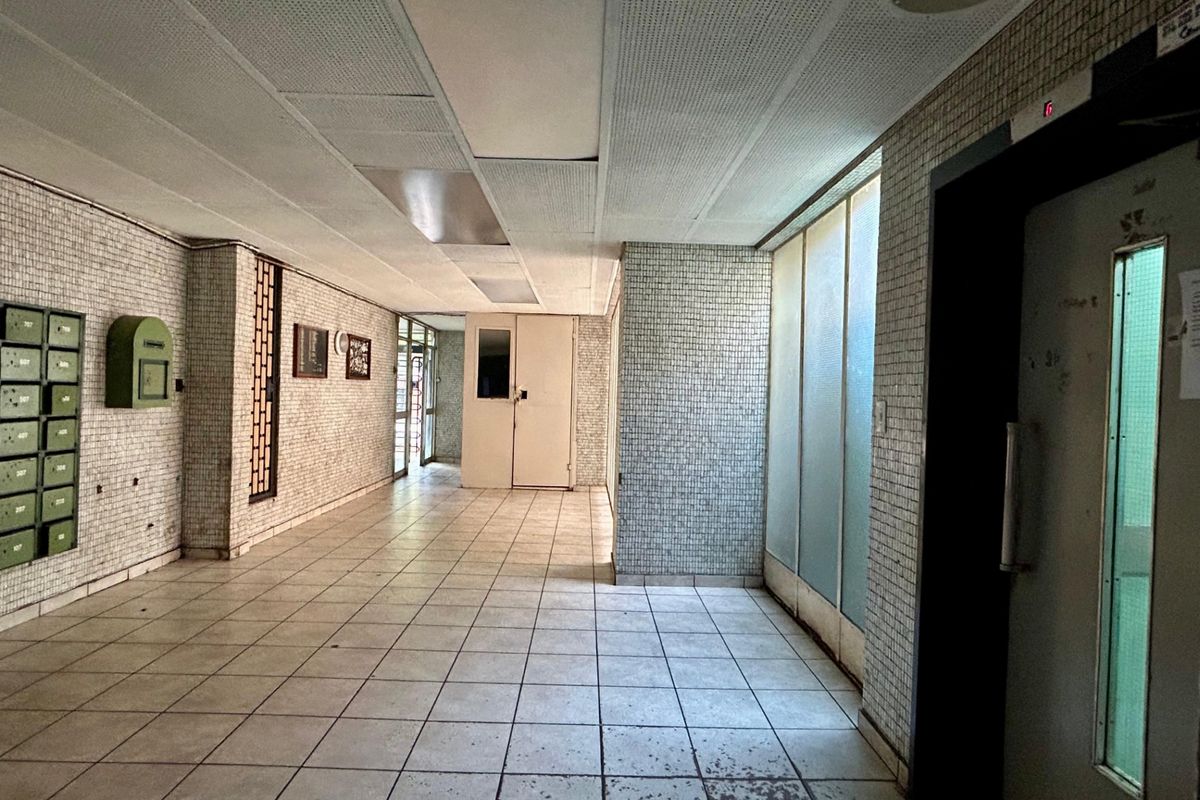 A communal apartment building entrance lobby featuring tiled walls and flooring, an elevator, and integrated mailboxes in a dated condition.