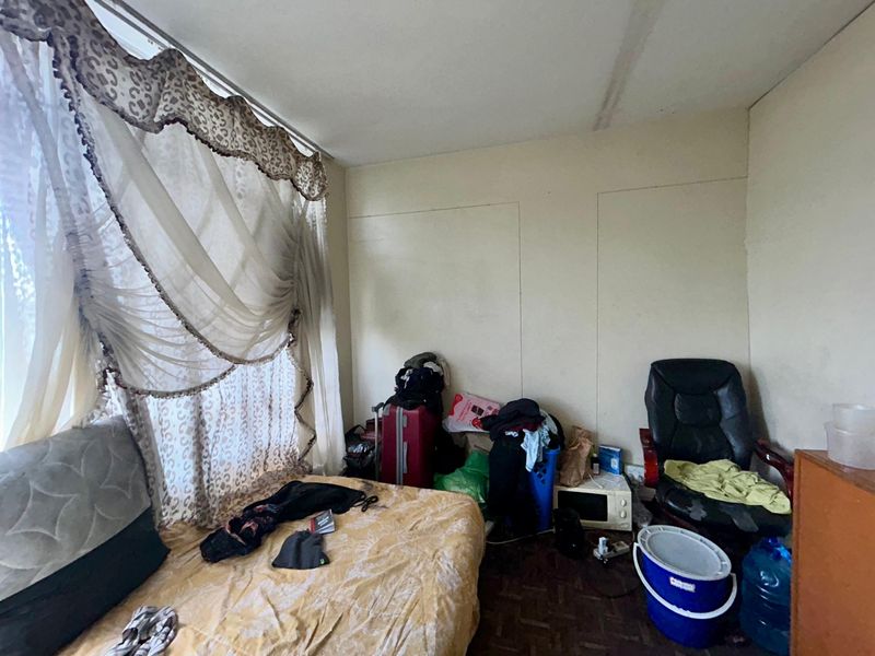 A bedroom featuring parquet flooring and a large window with decorative curtains, requiring cosmetic updates and maintenance to the ceiling and walls.