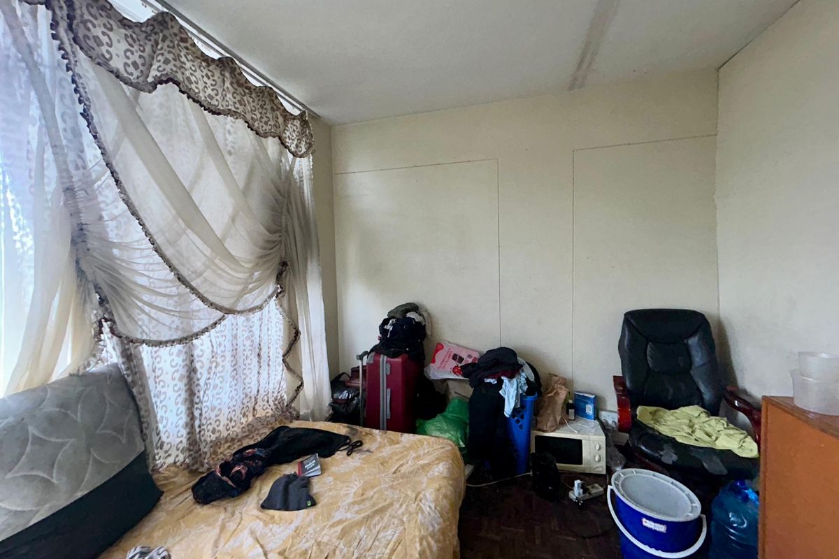 A bedroom featuring parquet flooring and a large window with decorative curtains, requiring cosmetic updates and maintenance to the ceiling and walls.