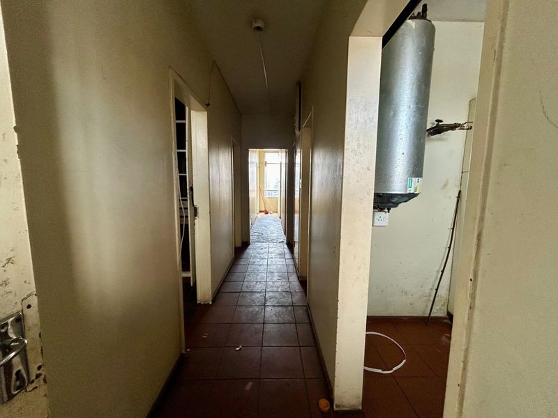 A vacant hallway featuring tiled flooring and a wall-mounted electric water heater, showing signs of wear and requiring cosmetic updates.