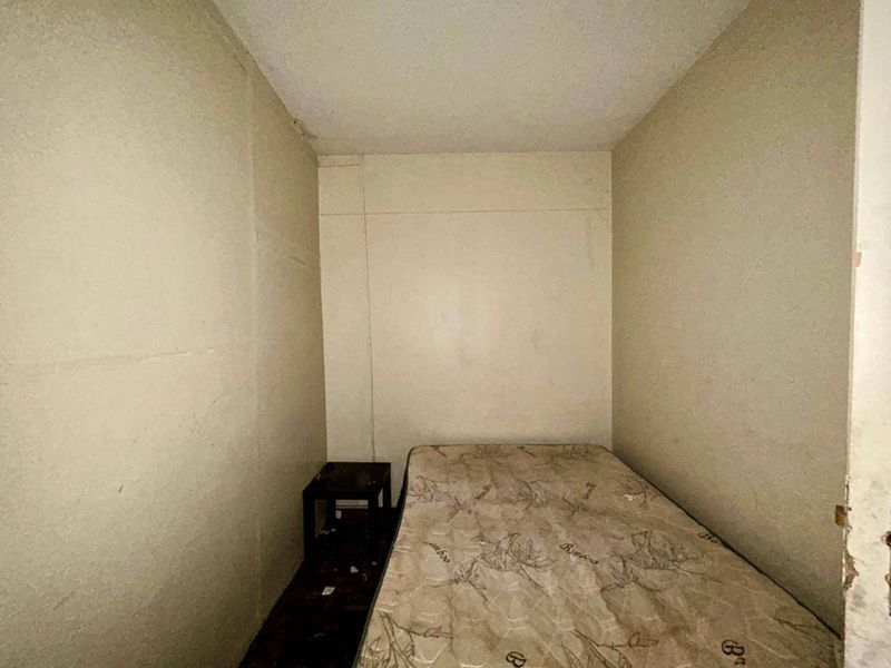 A small bedroom space requiring significant cosmetic updates, including wall repairs and flooring replacement to improve the overall condition.
