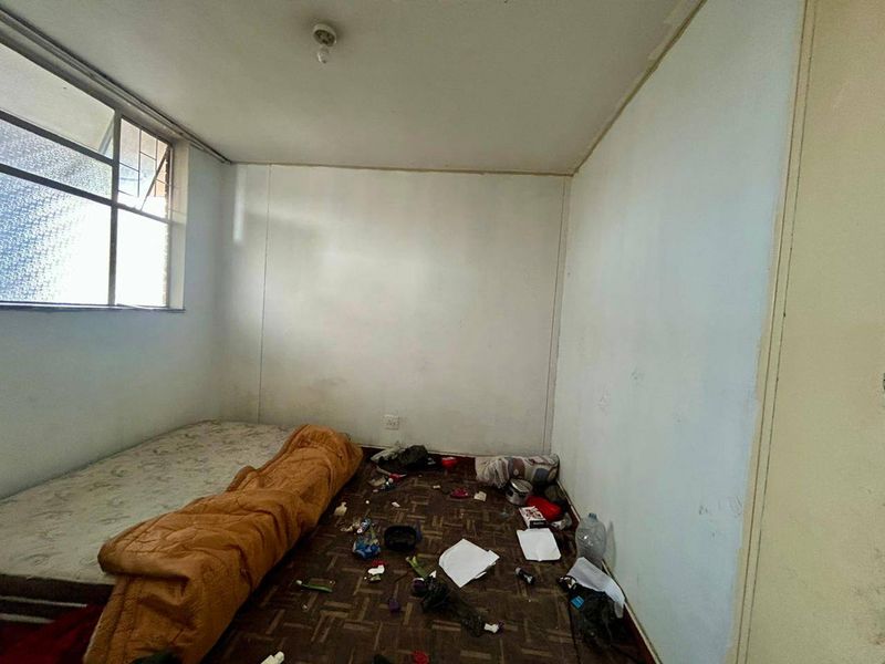 A bedroom space requiring significant renovation, featuring basic window fixtures and worn flooring, offering a blank canvas for potential refurbishment.