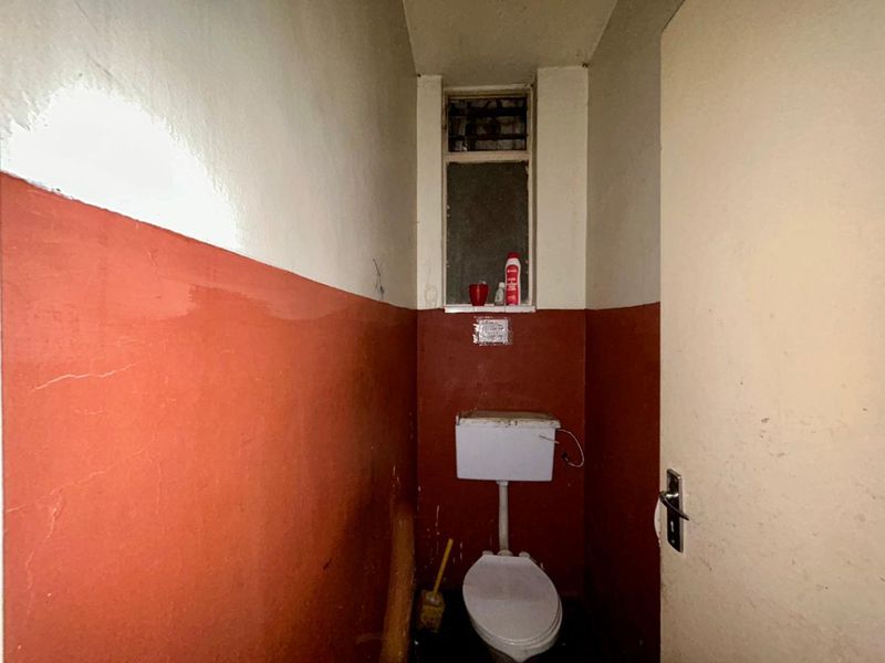 A small, dated bathroom featuring a standard toilet and window, requiring significant renovation and cosmetic updates to improve its condition.