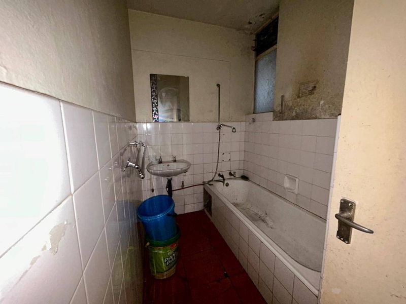 A dated bathroom featuring a bathtub and wall-mounted basin, requiring significant renovation and cosmetic updates to restore functionality and appeal.
