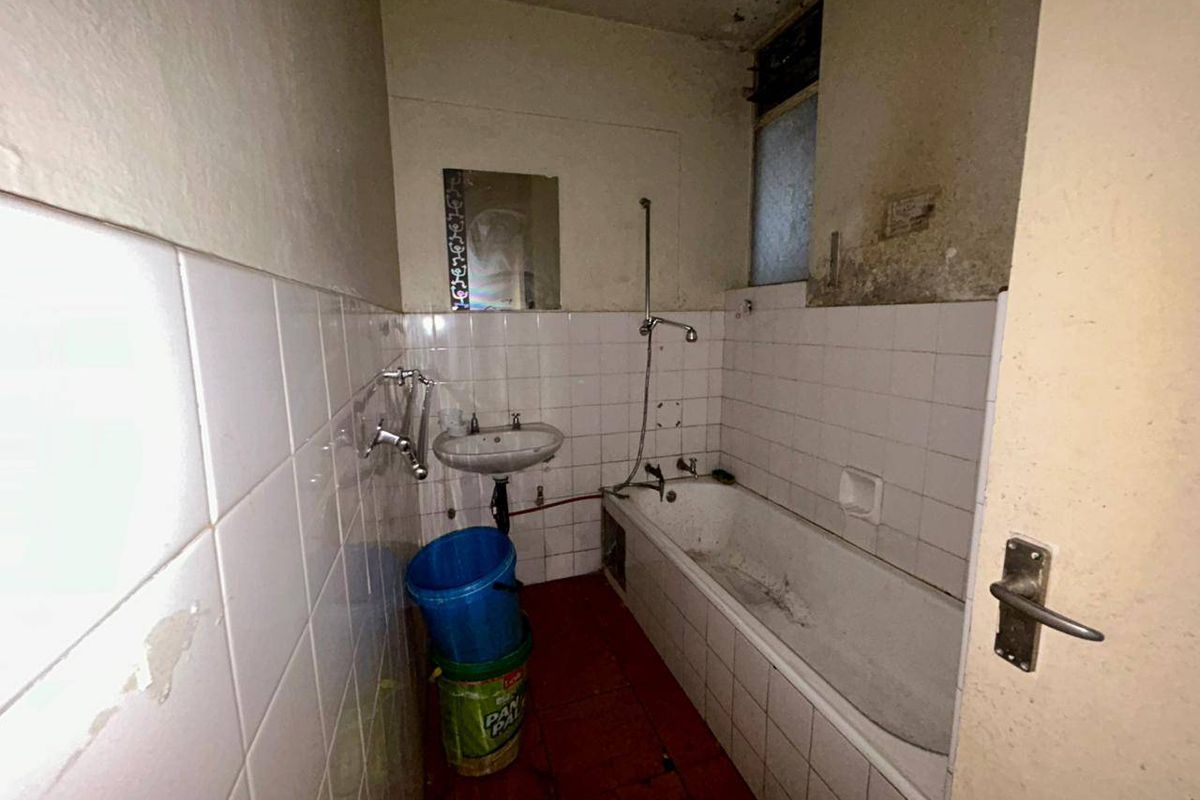 A dated bathroom featuring a bathtub and wall-mounted basin, requiring significant renovation and cosmetic updates to restore functionality and appeal.