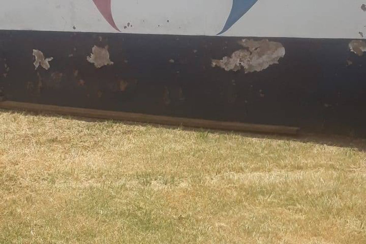 A rear exterior view of a perimeter wall featuring a painted mural and security razor wire, set against a grassed area.