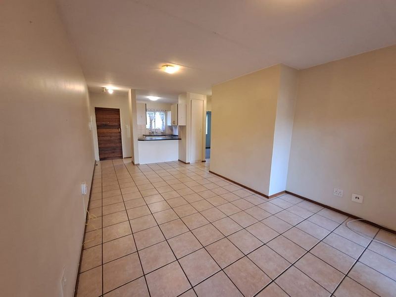 An open-plan living and kitchen area featuring neutral tiled flooring, built-in cabinetry, and a functional layout, presented as a vacant space.