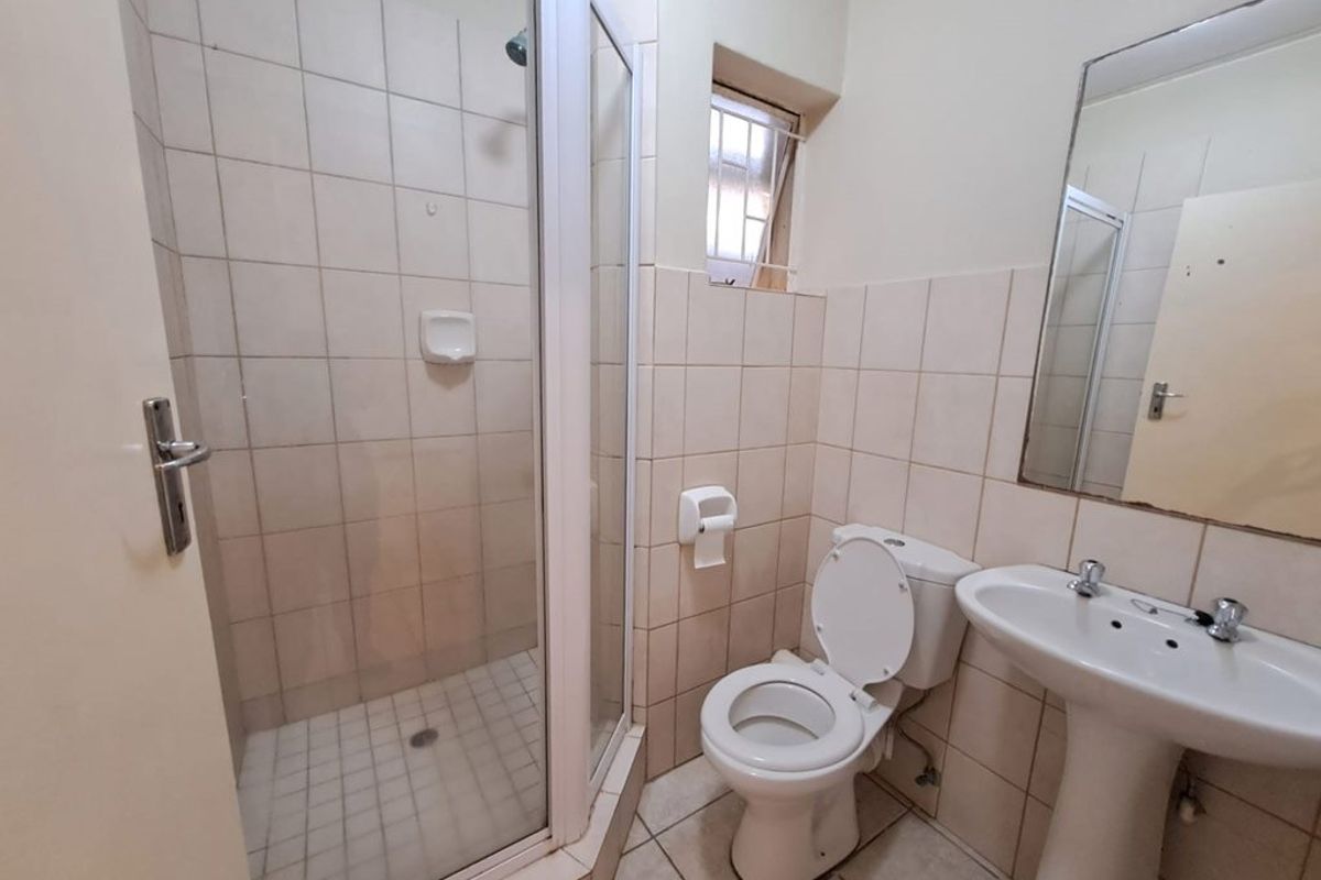 A functional bathroom featuring a shower enclosure, pedestal basin, and toilet with neutral wall and floor tiling.