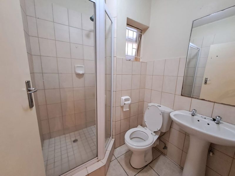 A functional bathroom featuring a shower enclosure, pedestal basin, and toilet with neutral wall and floor tiling.