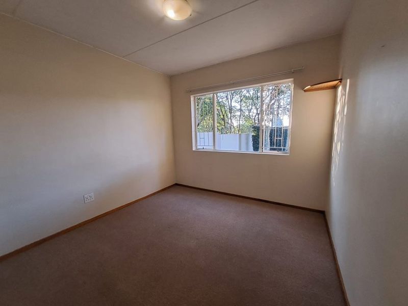 A clean, empty bedroom featuring neutral walls, carpet flooring, and a window fitted with security bars, offering a blank canvas for personalization.