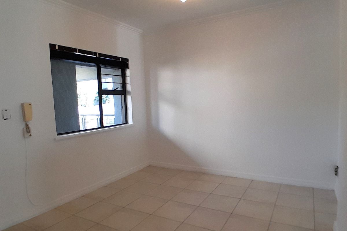 An empty, neutrally painted living area featuring tiled flooring, a ceiling light fixture, and an intercom system.