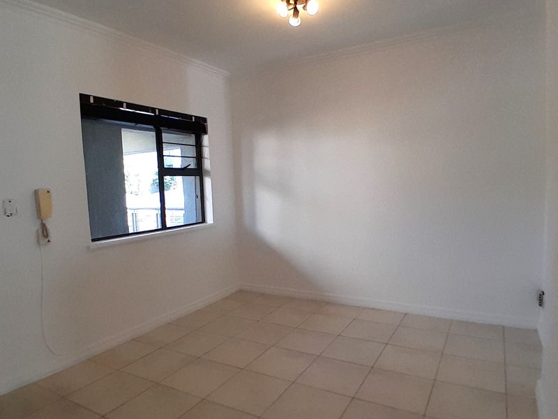 An empty, neutrally painted living area featuring tiled flooring, a ceiling light fixture, and an intercom system.
