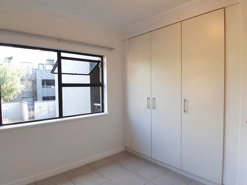 A clean, empty bedroom featuring neutral tiled flooring, built-in cupboards, and an aluminium-framed window providing natural light.