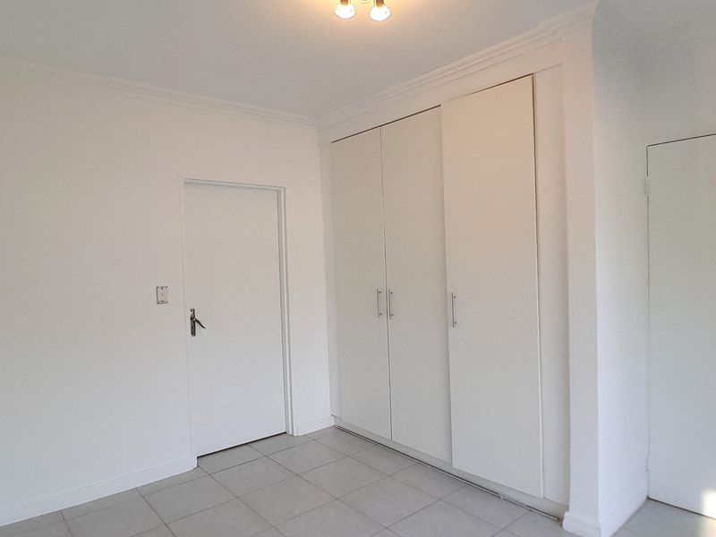 A clean, empty bedroom featuring neutral tiled flooring, built-in cupboards, and crisp white walls, offering a versatile space ready for personalization.