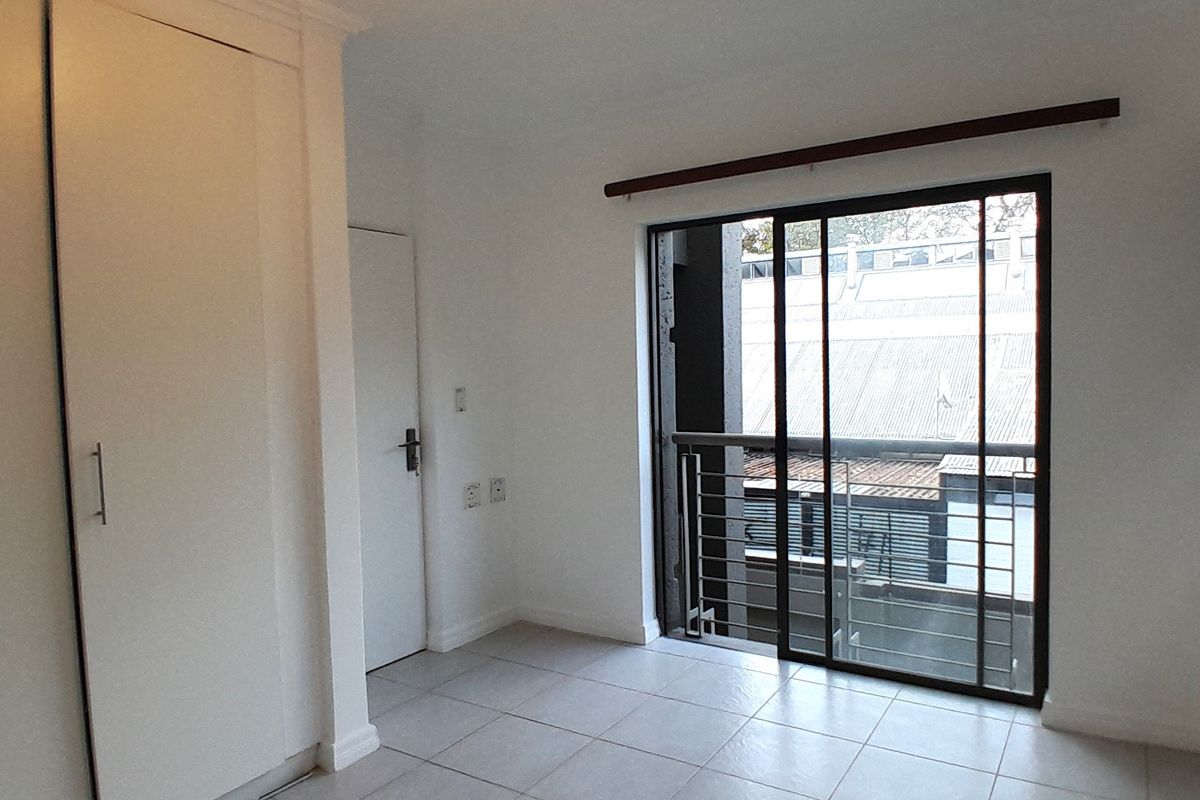 A bright, empty bedroom featuring tiled flooring, built-in cupboards, and a sliding glass door leading to a balcony.