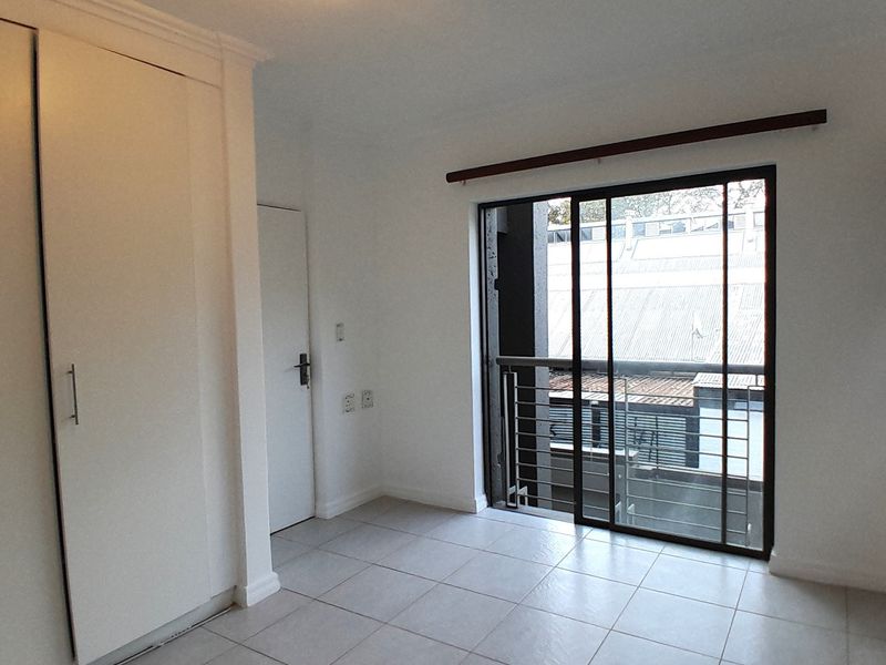 A bright, empty bedroom featuring tiled flooring, built-in cupboards, and a sliding glass door leading to a balcony.